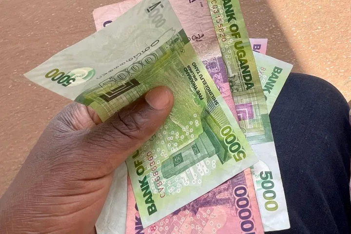 A hand holding Ugandan shilling notes